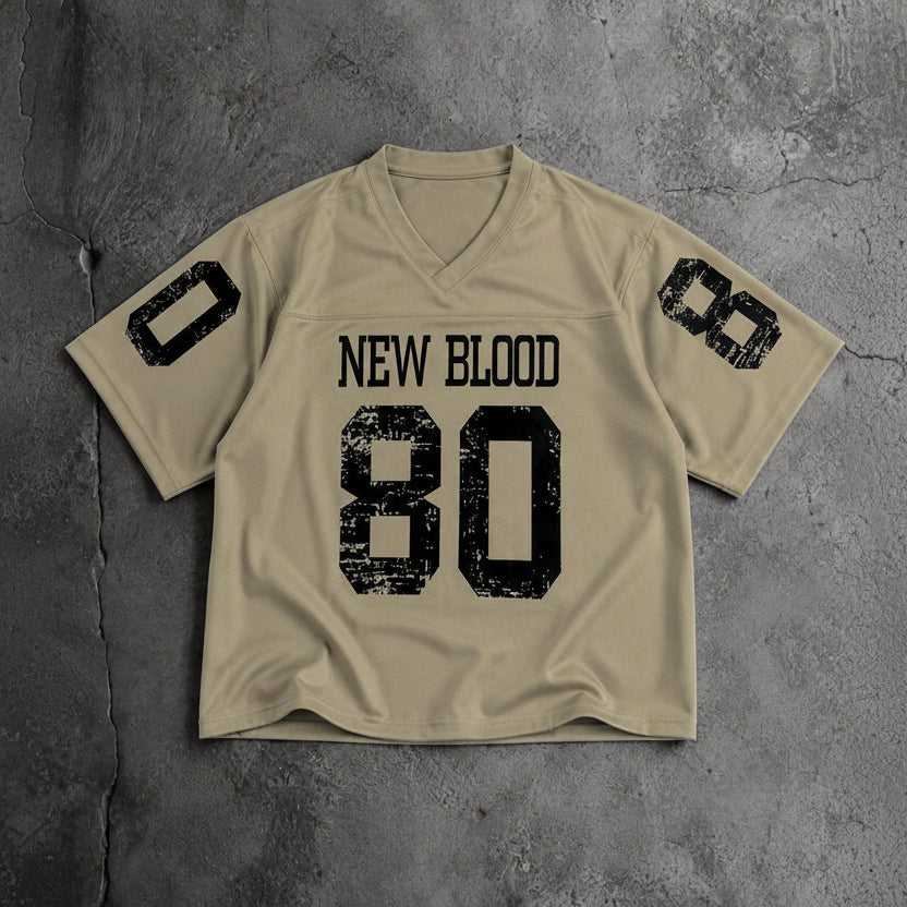 A beige short-sleeve football-style jersey laid flat on a textured gray surface, with distressed black text reading 'NEW BLOOD' and large '80' on the front, plus black '0' and '8' graphics on the sleeves.
