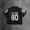 A black short-sleeve football-style jersey laid flat on a textured gray concrete surface. The front has distressed white text reading 'NEW BLOOD' above a large distressed white '80'.