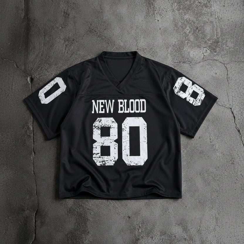A black short-sleeve football-style jersey laid flat on a textured gray concrete surface. The front has distressed white text reading 'NEW BLOOD' above a large distressed white '80'.