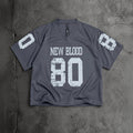 A dark gray v-neck athletic jersey with distressed white text reading 'NEW BLOOD' and the number '80' on the front, plus matching white numbers on the sleeves, laid flat on a textured gray concrete surface.